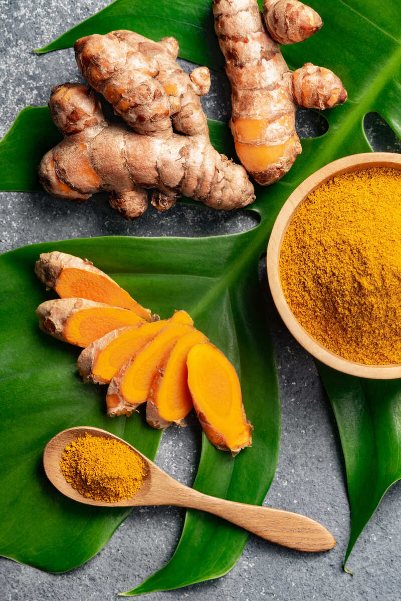 rhizomes de curcuma découpés avec poudre curcuma sur feuille verte